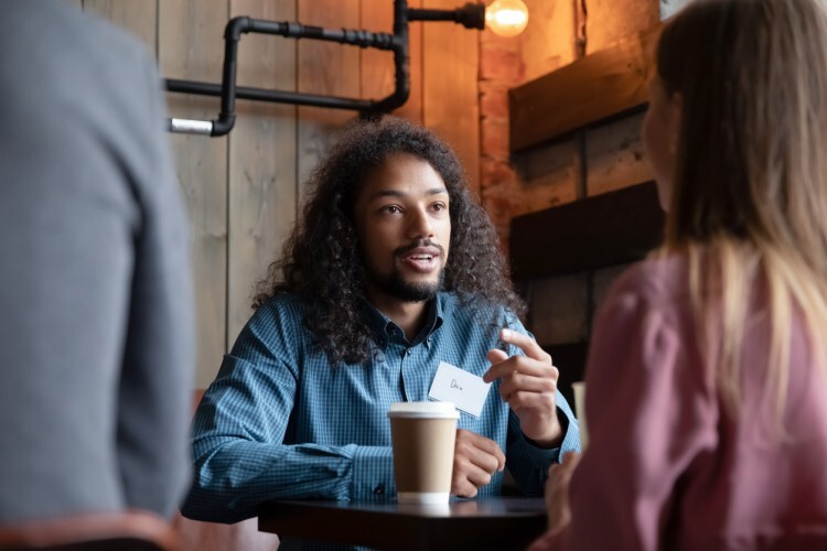 A person seated at a table wearing a nametag is having a conversation with two other people.