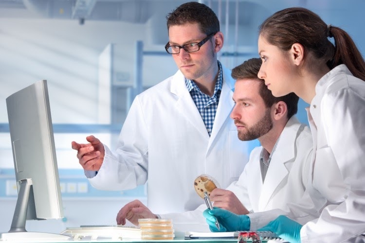 Three people in lab coats look at a computer screen.