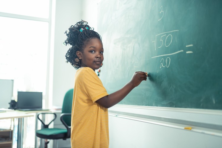 A young student solves a math problem on a chalkboard.