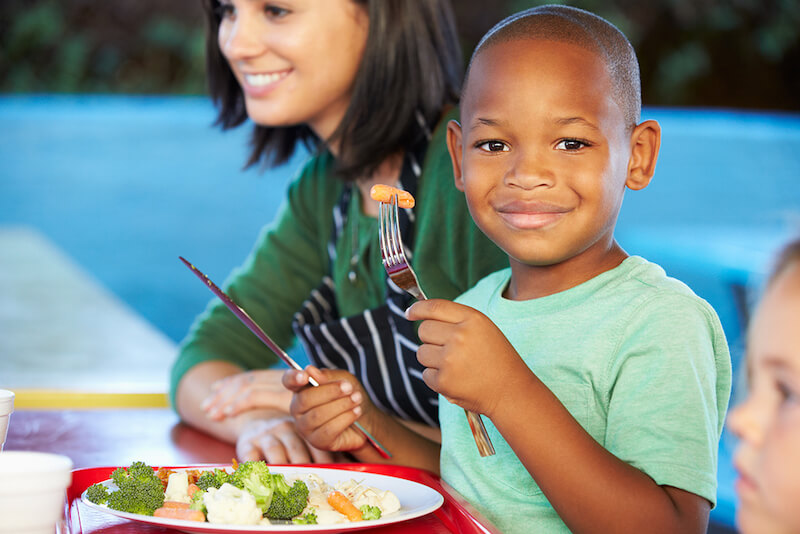 A smiling child eating a healthy lunch.