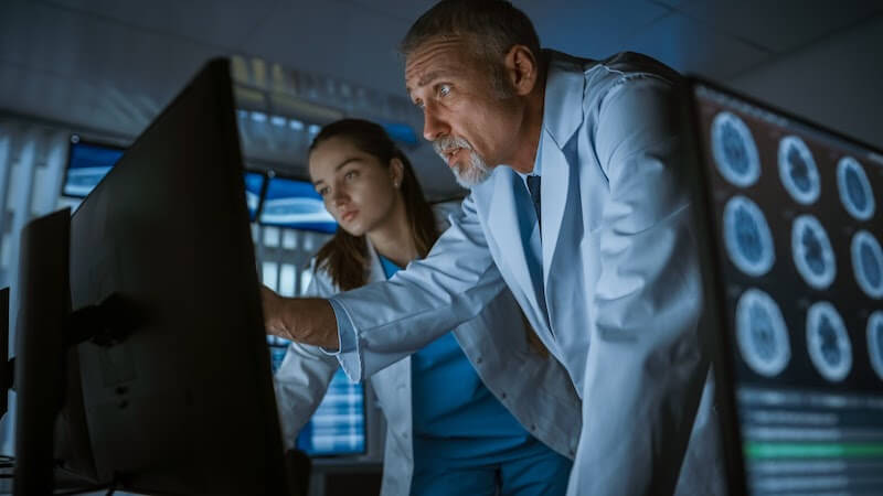 Two medical researchers use healthcare analytics in neuroscience at large computer displays.