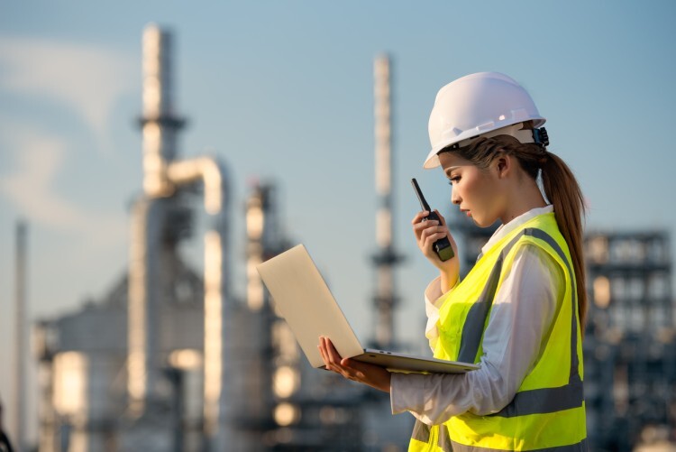 An industrial hygienist with a laptop communicates about safety hazards at a factory site.