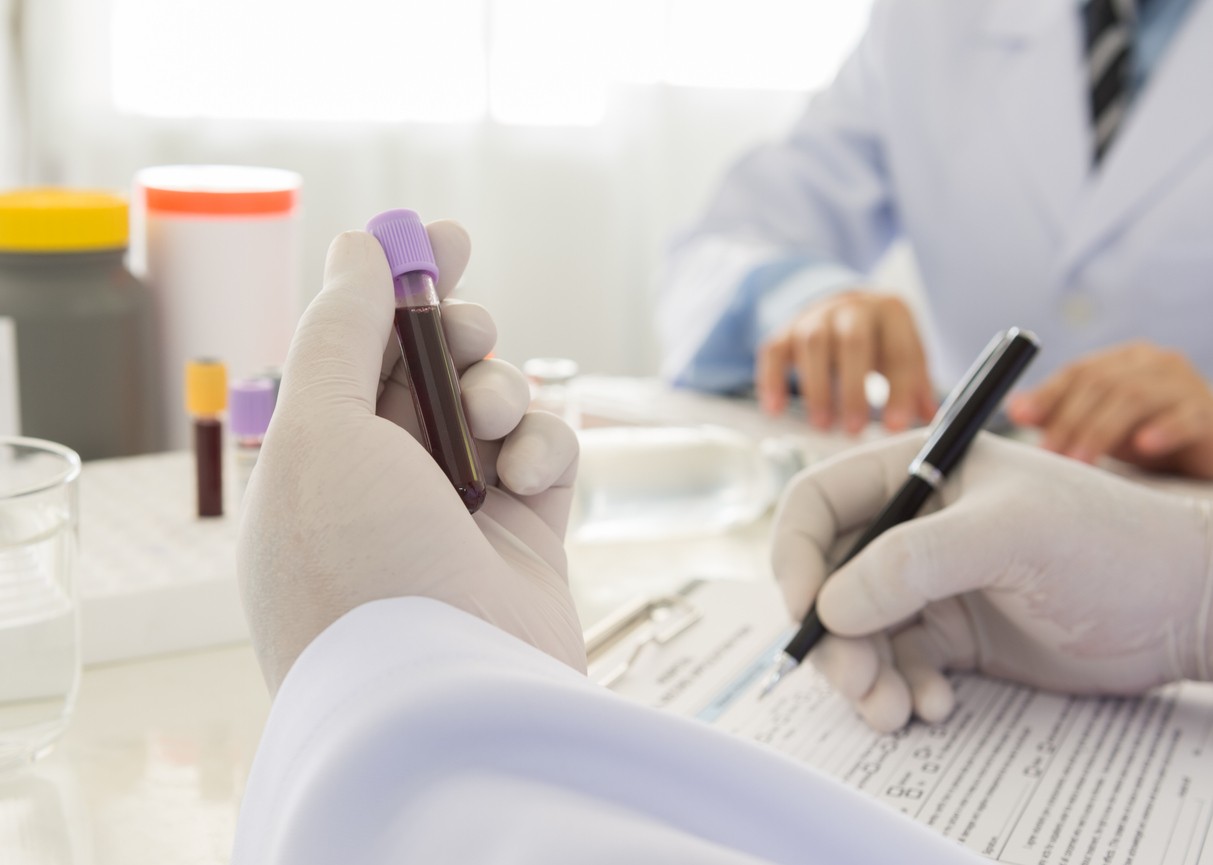 Two doctors in white lab coats examine a test tube containing a blood sample.