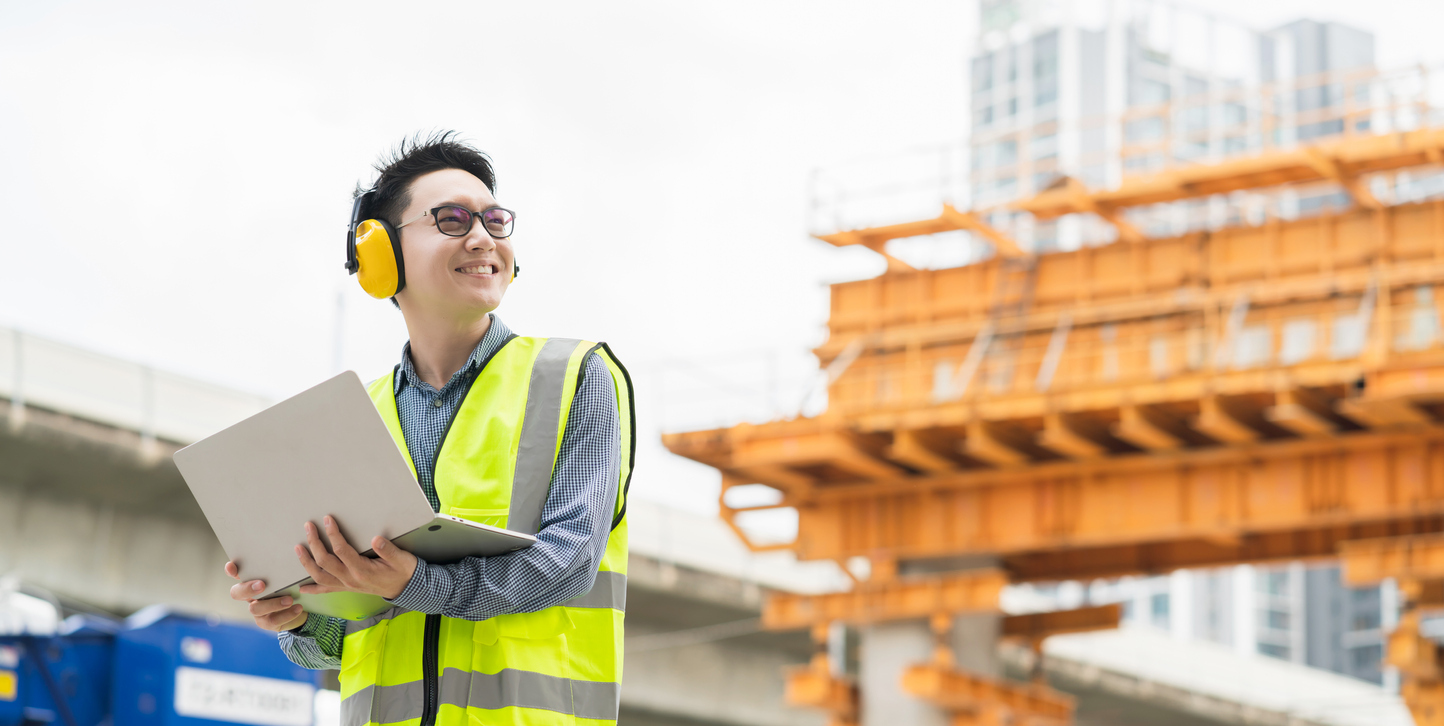 A person holding a laptop stands in a construction site.