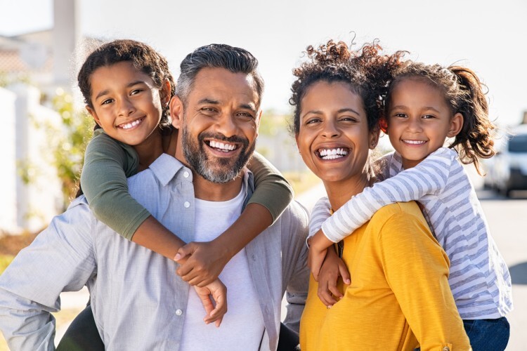 A smiling family, two adults and two children, gather in the community.