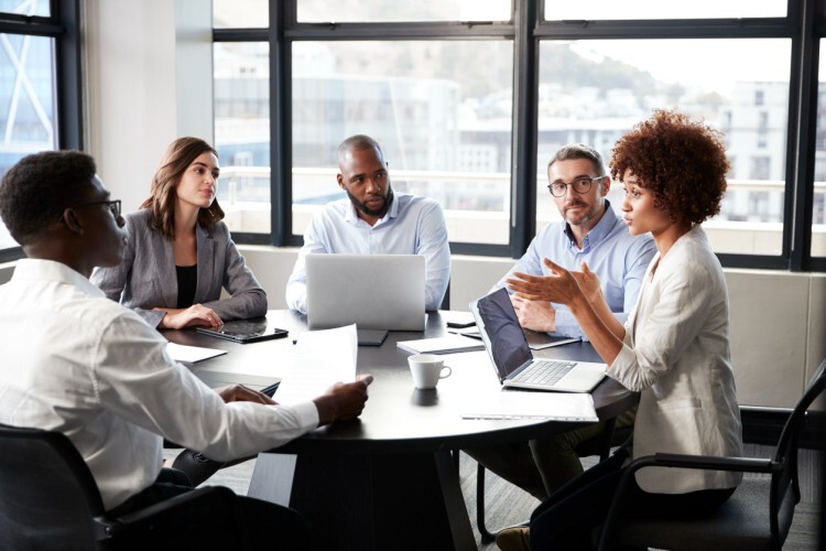 A public health analyst leads a team meeting at a conference table in an office.