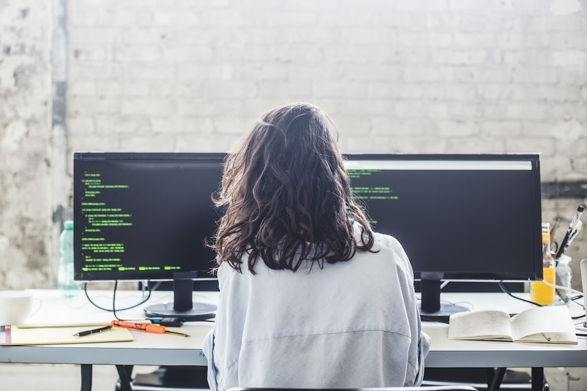 A woman writes code at a desk in an open office.