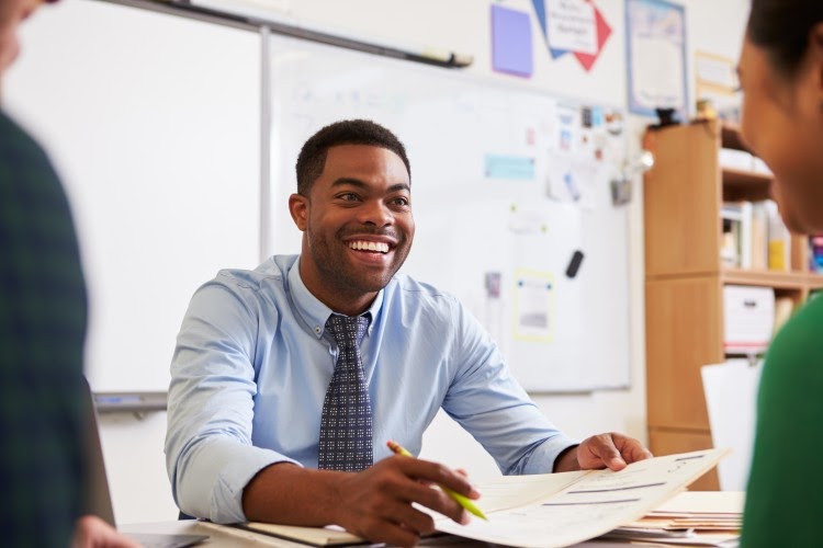 A smiling teacher meets with a student.