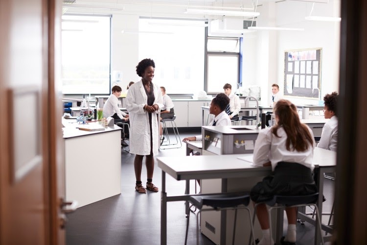 A science teacher wearing a lab coat presents a lesson to the class.