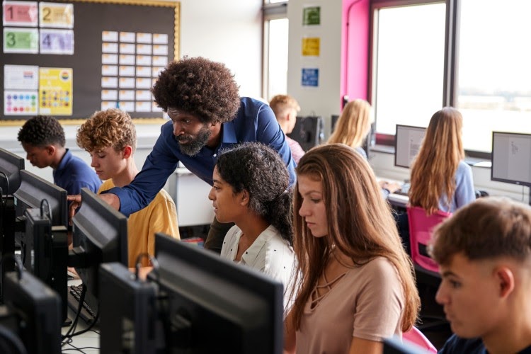 A teacher helps students working in a computer lab.