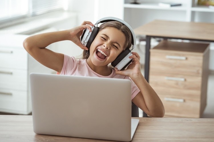 A student wearing headphones sings along to music while sitting at a laptop.