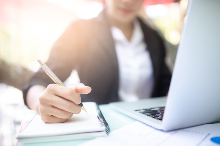 A curriculum specialist working with a laptop, pen, and paper.