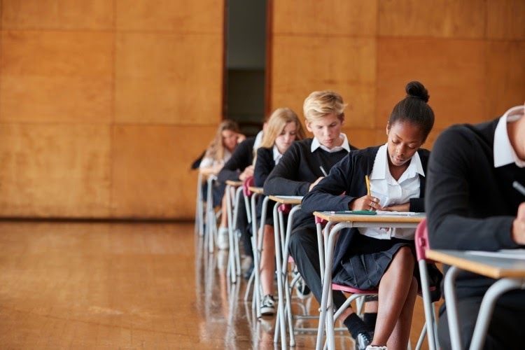 Students in uniform sit in a row of desks taking an exam.