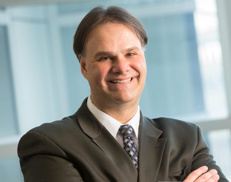 A male healthcare professional wearing a white lab coat and face mask looks away from the camera.