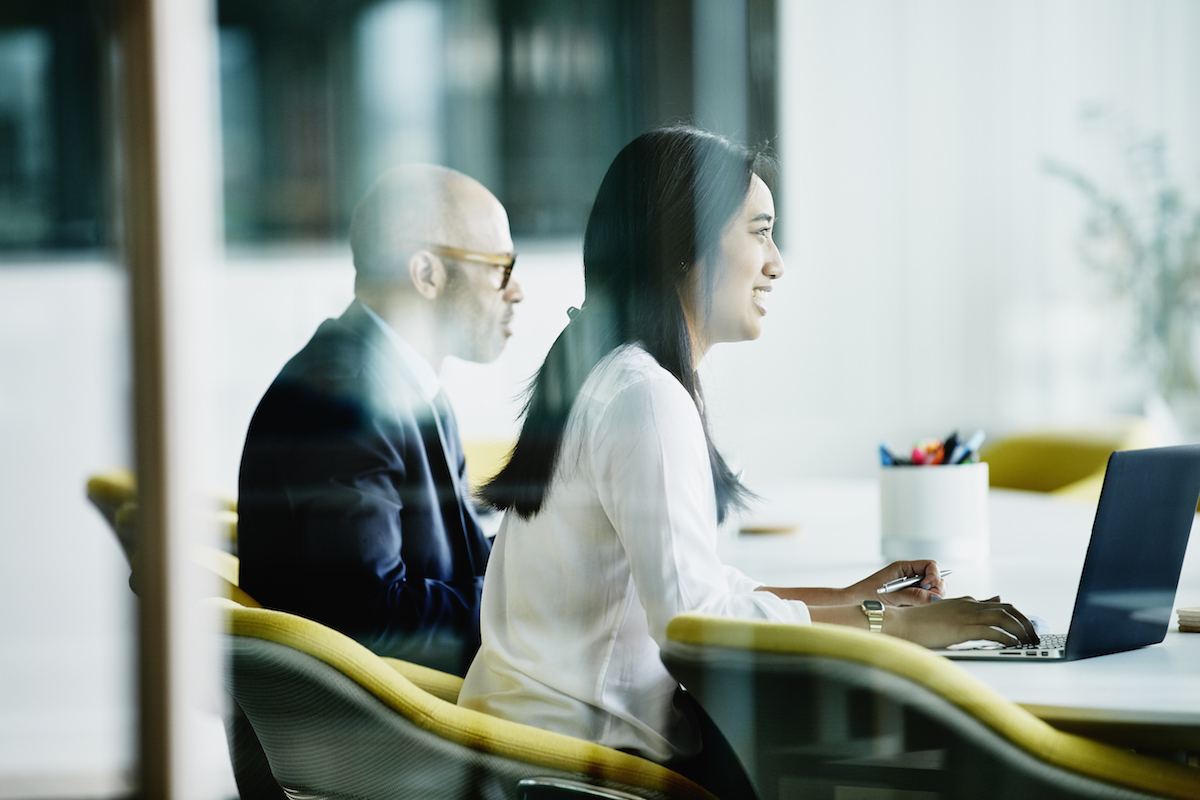 Two colleagues smile as they sit at a table in a conference room.