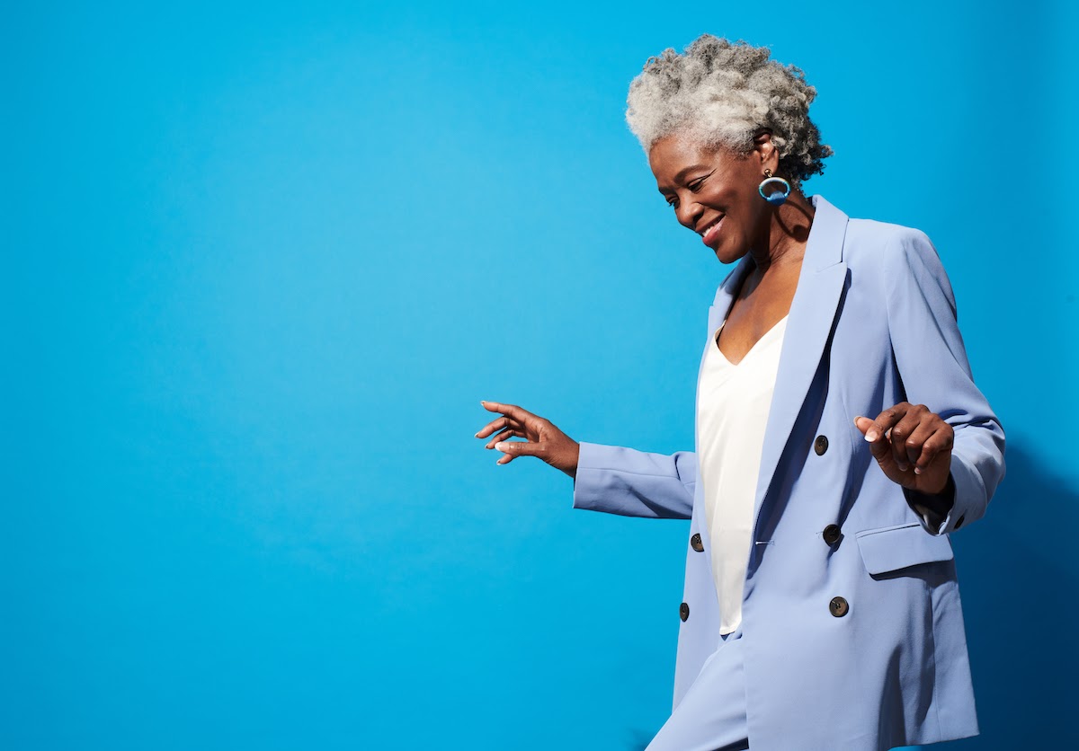 A professional woman in a light blue suit smiles, looking down against a bright blue background.